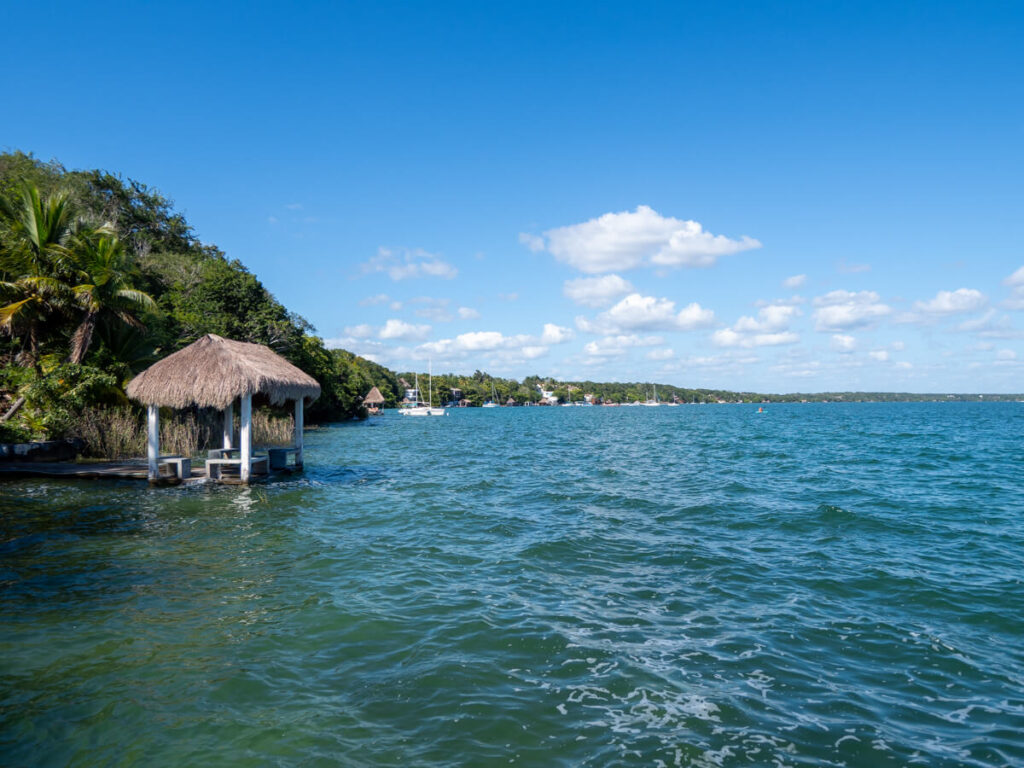 Bacalar Lagoon stretching out into the distance. The water's edge is lined with greenery and small docks.