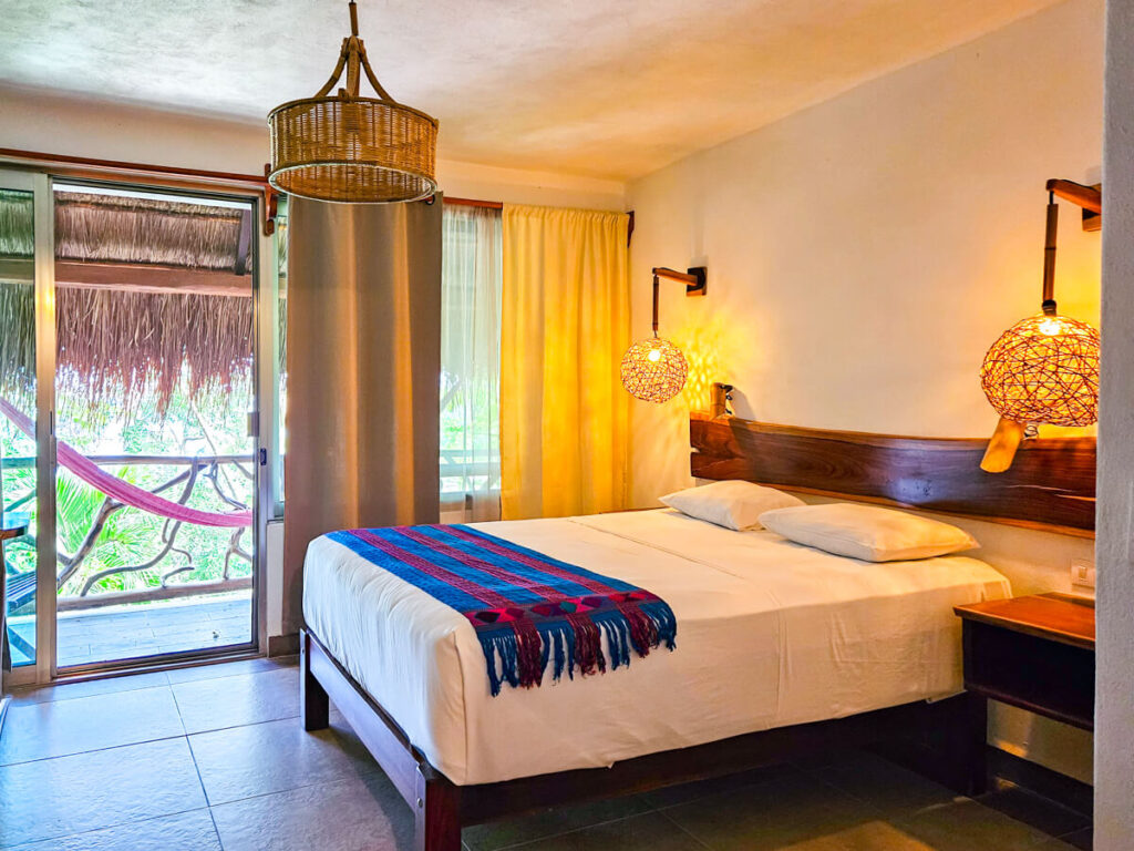 A bedroom at the Eco-hotel Casa Lamat as viewed from the door. There is a double bed with lights on either side, and outside there is a private balcony with a hammock.