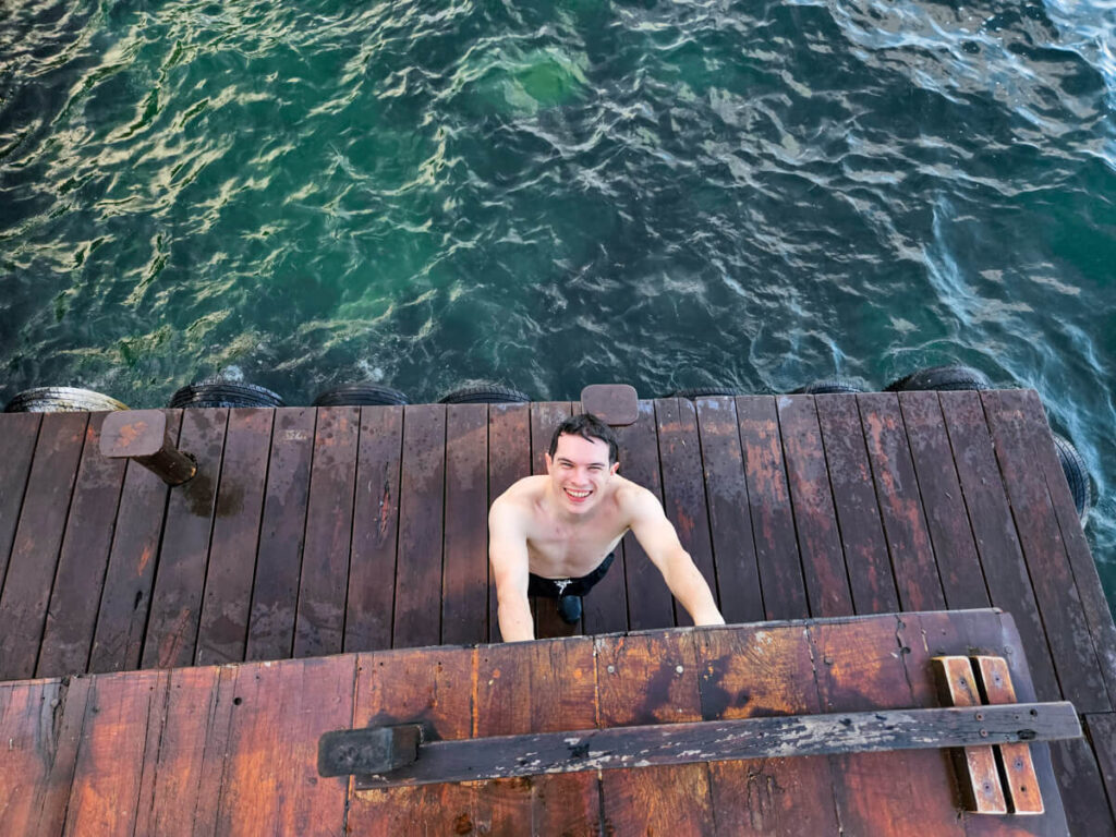 Dan standing at the bottom of a wooden ladder on a platform at Casa Lamt after jumping into the cool waters of Bacalar Lagoon.