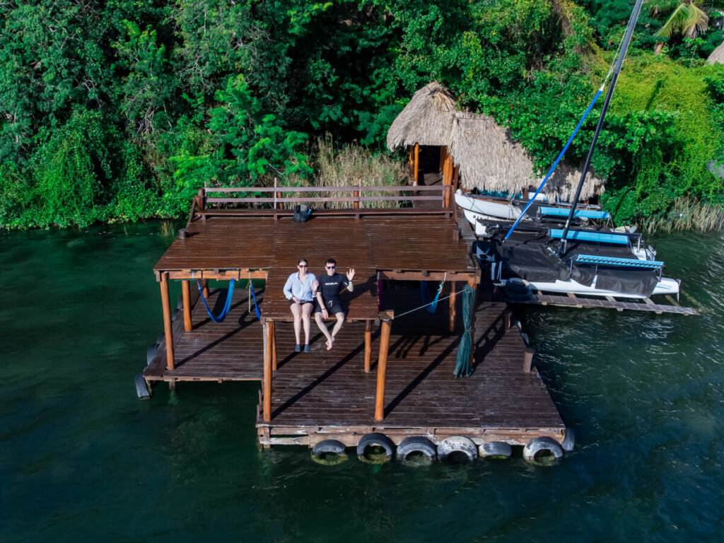 Dan and Lucy waving at their drone as it flys low over Bacalar Lagoon in front of the Eco-Hotel Casa Lamat.