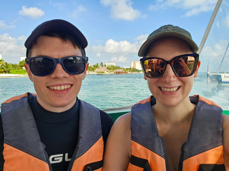 Dan and Lucy sitting on a boat on their way to Isla Contoy with Ocean Tours. They are wearing lifejackets, sunglasses and caps.