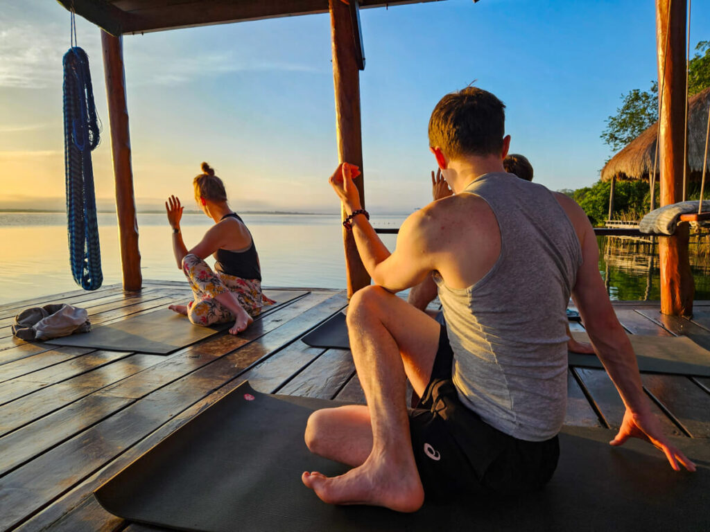 Dan stretching in a seated position at a yoga class at Casa Lamat. The class is being held on a dock on Bacalar Lagoon at sunrise.