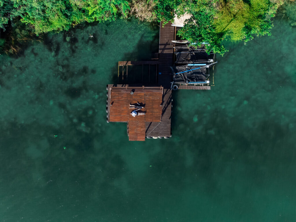 Dan and Lucy lying down on a wooden dock on Bacalar Lagoon, as viewed from a drone.