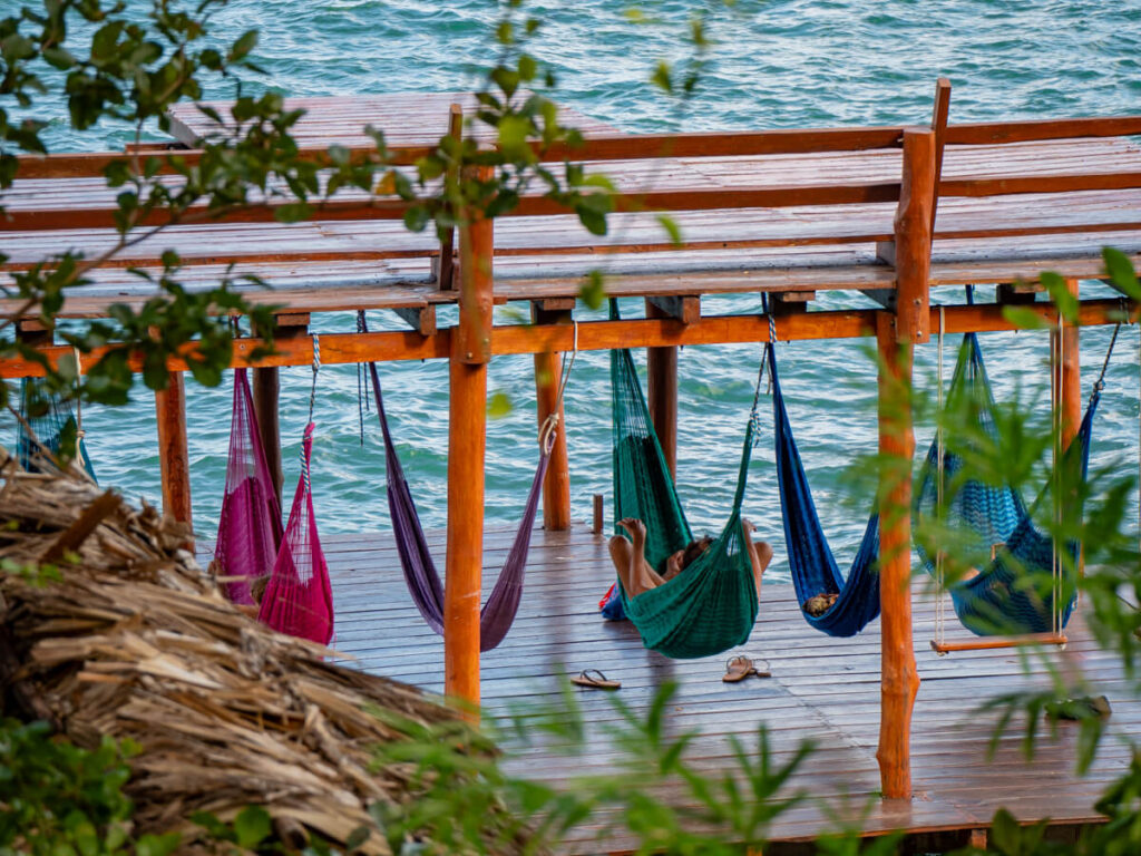 People relaxing on colourful hammocks hanging from the dock at Eco-Hotel Casa Lamat in Bacalar.