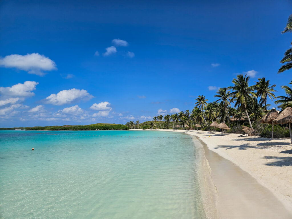 A completely empty beach on Isla Contoy, a popular day trip from Cancún. The sky is a clear blue and the water is light and calm.