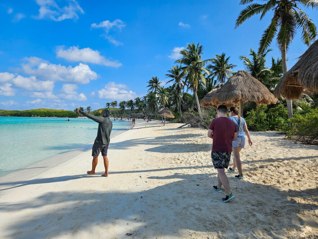 Tlal, an Ocean Tours guide, leading a small group around Isla Contoy. Palm trees line the pristine white sand beach.