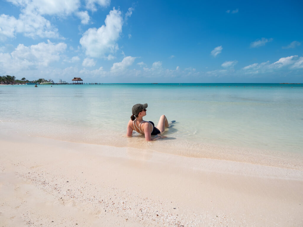 Lucy sitting on Isla Contoy Beach in the shallow water. The sand is white and clean, and the water is clear and blue.
