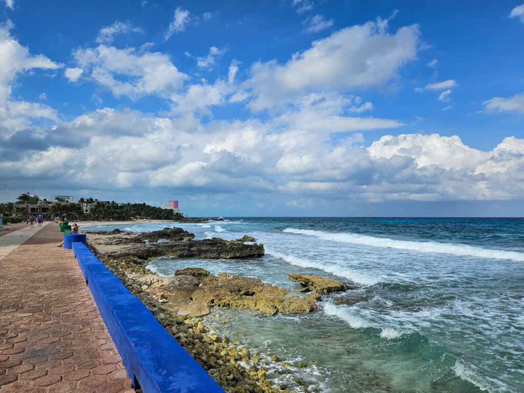 A seaside walkway lined by a colourful wall with views of the sea crashing on the shore on the coast of Isla Mujeres.