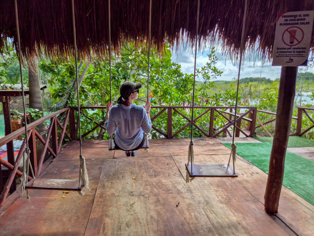 Lucy relaxing on a swing surrounded by greenery and looking out at Los Rapidos, Bacalar.