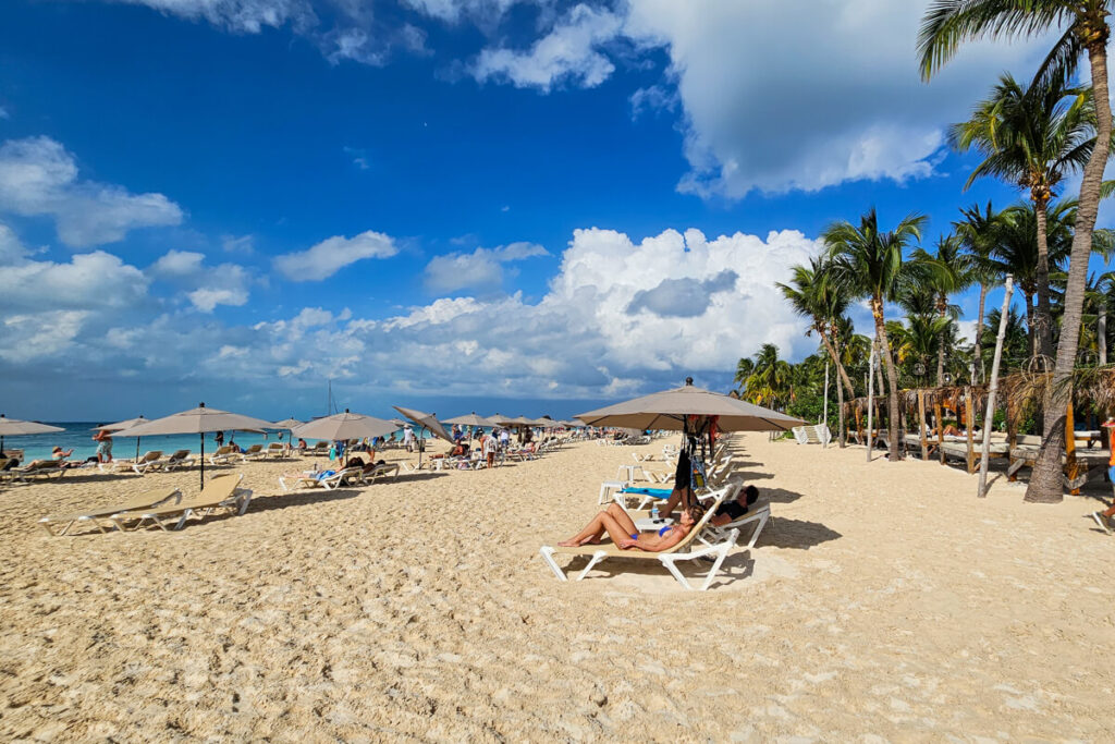 People lounging on sun chairs at a palm-fringed beach club in Isla Mujeres, Mexico.