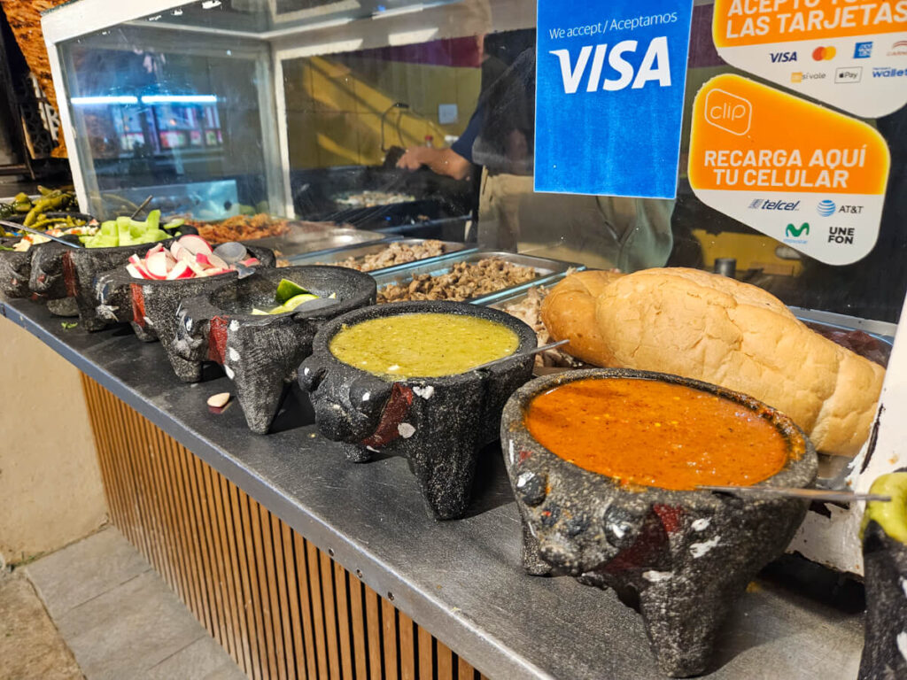 Pots filled with sauces and salad in front of a food vendor stall in Parque de las Palapas, Cancún.