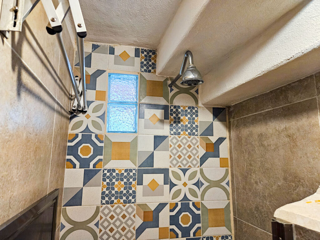 A shower with colourful and patterned tiles on the wall.