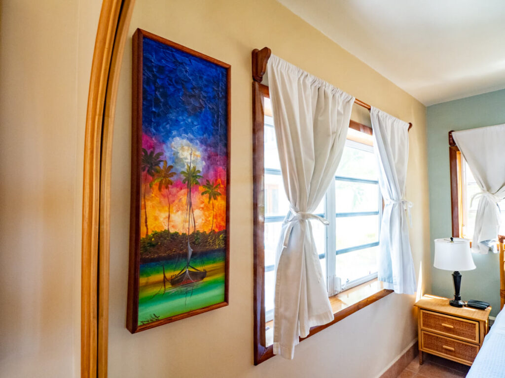 A colourful painting of sailboat in calm waters hanging on the wall of a bedroom at Belizean Shores Resort.
