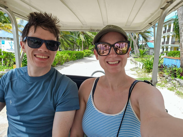 Dan and Lucy smiling as they drive a golf cart down a quiet street in San Pedro, Belize. A golf cart is the most popular way to get around Ambergris Caye.