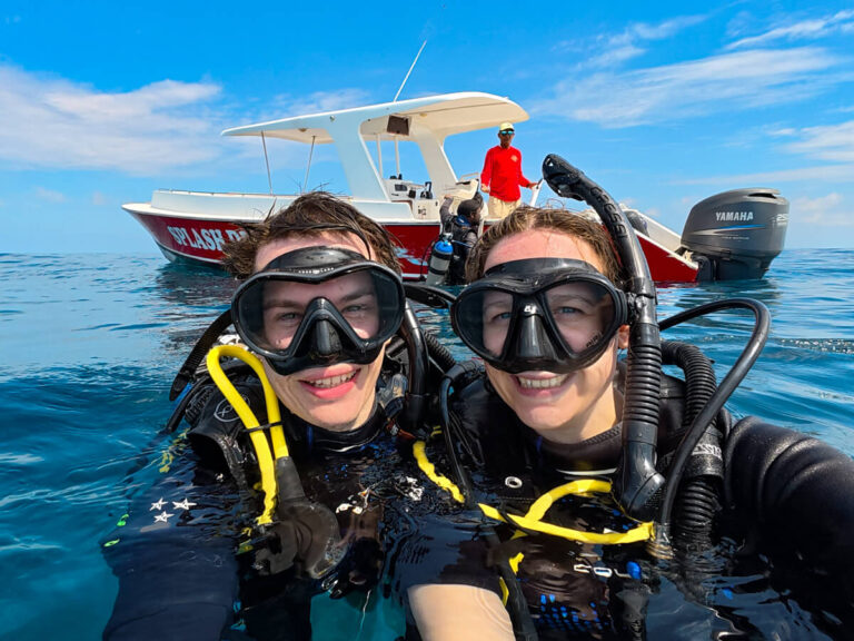 Dan and Lucy at the surface after SCUBA diving in Belize. They are smiling and wearing dive masks and black SCUBA gear.