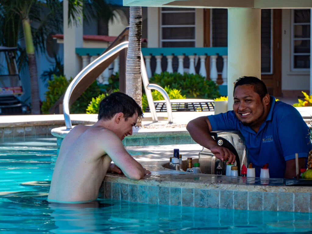 Dan laughing with a bartender at Belizean Shores Resort as he leans on the pool bar.