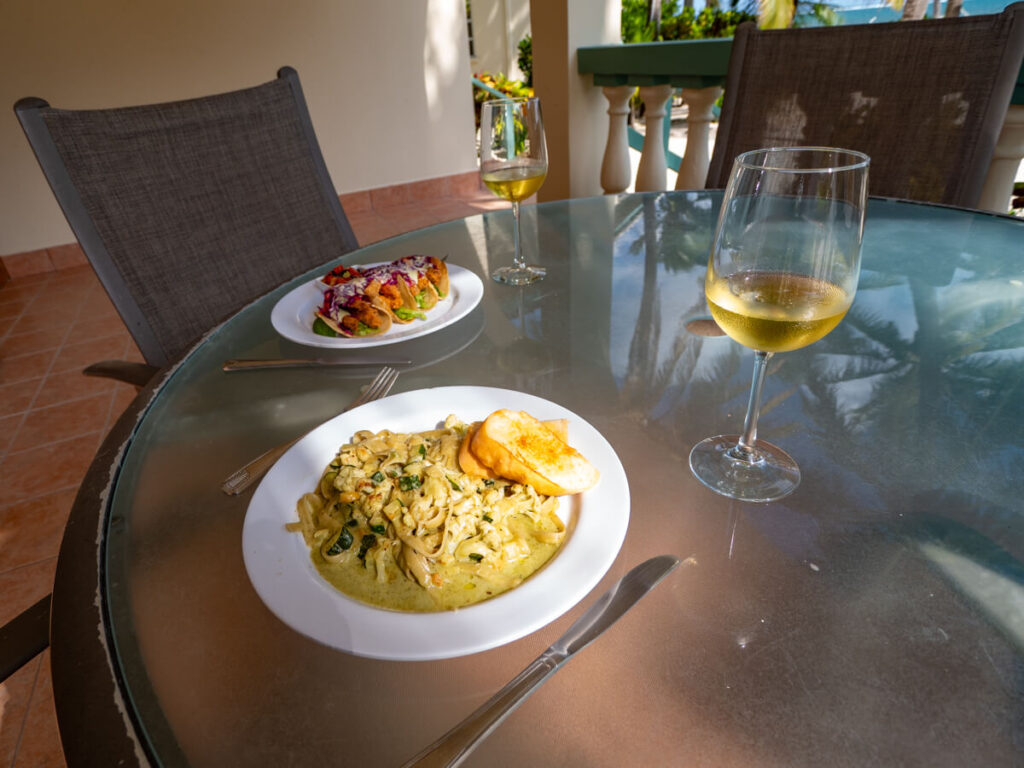 A plate of fresh tacos, a bowl of pasta, and two glasses of wine set out on a table in the sunshine at Belizean Shores Resort.