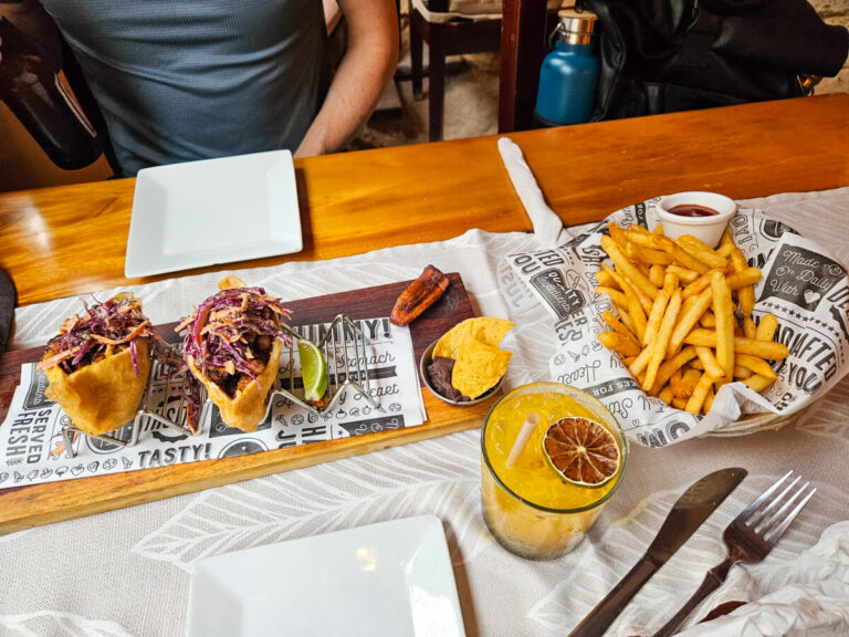 A spread of food at Elvi's Restaurant in San Pedro, Belize. There is a portion of fry jacks, fries, re-fried beans, plantains, and a margarita cocktail.