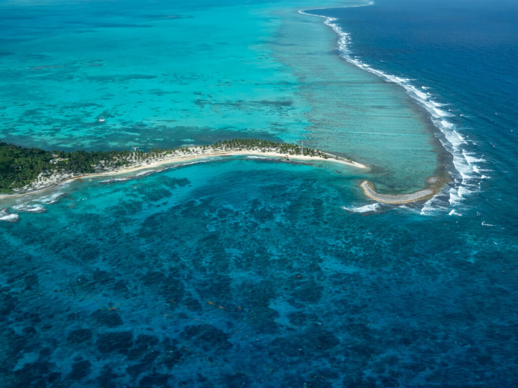 The curved coast of a remote island in Belize in clear, blue waters. This photo was taken from a plane.