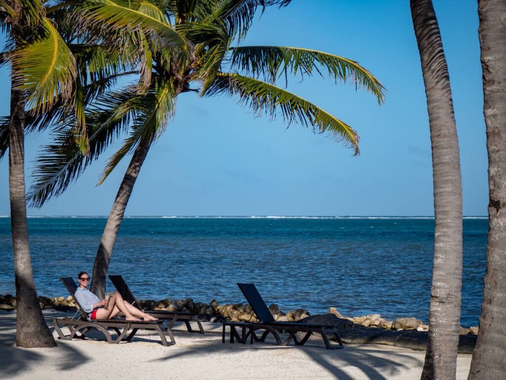 Lucy sat on a sun lounger with a cocktail in hand. She is on the beach at Belizean Shores Resort.