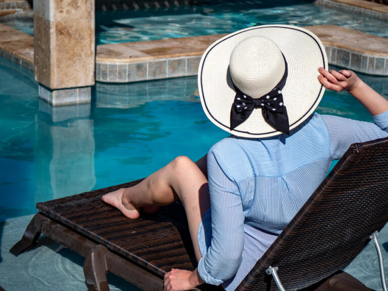 Lucy sitting in a sun lounger in a big white hat looking out over the pool at Belizean Shores Resort.