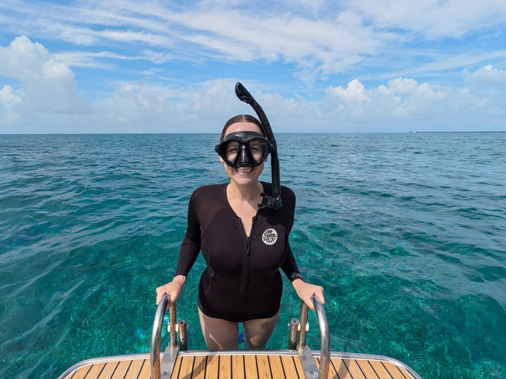 Lucy smiling in her snorkelling gear as she climbs down a boat ladder into crystal clear waters.