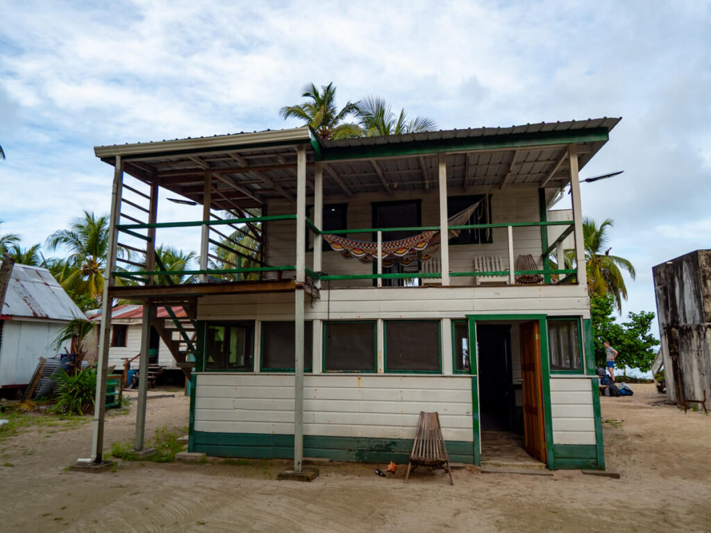 The Ragga Residence on Tobacco Caye. A two-storey wooden structure with hammocks hanging on each side, and painted walls of white and green.