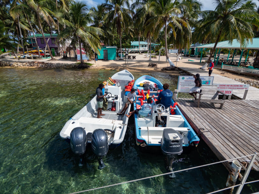 Two small motor boats docked on the small dock at Tobacco Caye. A few crew members are relaxing on the boats in the sunshine.