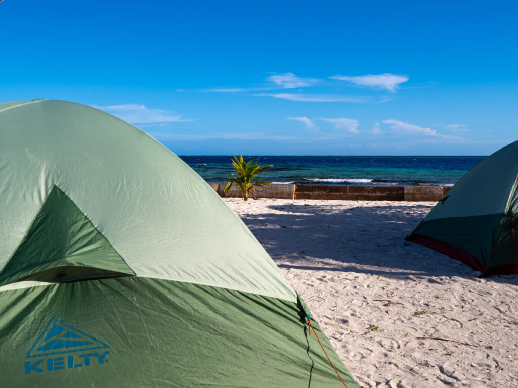 Camping on Rendezvous Caye. A couple of basic tents are set up on the sand and looking out at the Pacific Ocean.