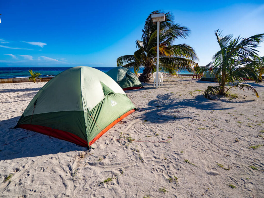 The morning after camping overnight on Rendezvous Caye, Belize. A few tents set up on the sand on a clear, sunny morning.