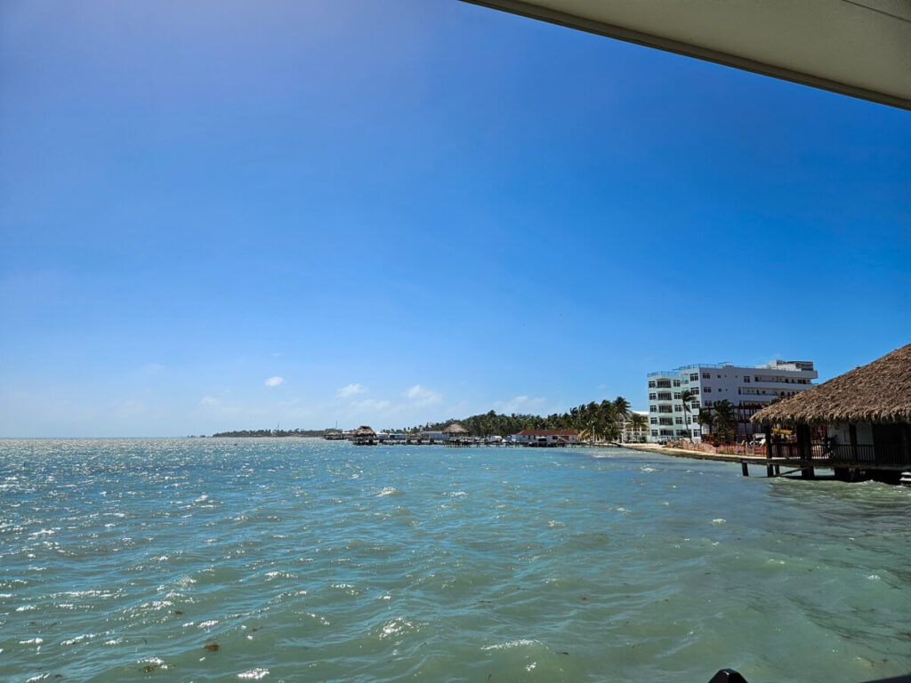 The view across the ferry dock in San Pedro. The sun is high in the sky, and the coast is lined with palapas and palm trees.