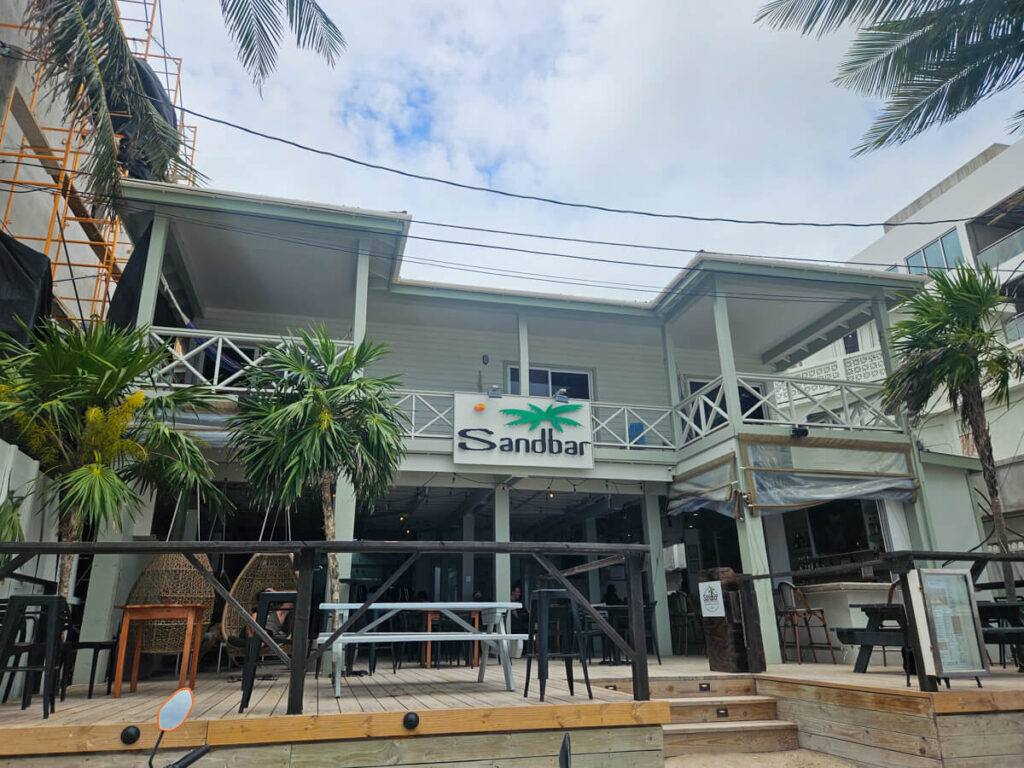 The welcoming entryway to Sandbar Beachfront Hotel and Restaurant in San Pedro, Belize. A few small steps lead up to a decked dining area, perfect for a drink in the afternoon sunshine.