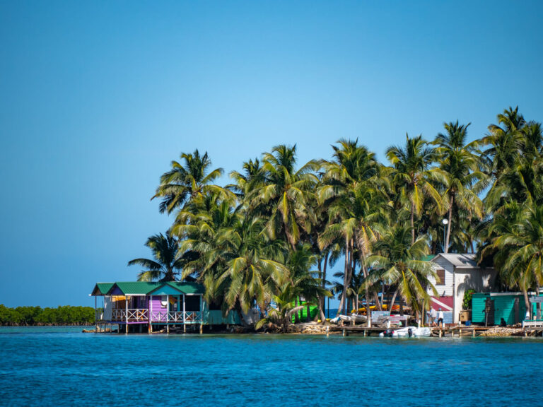 Colourful overwater bungalows, surrounded by swaying palm trees, on Tobacco Caye, Belize.