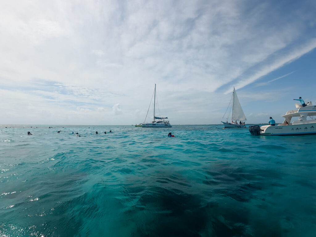 A handful of small boats moored in the shallow waters of the Hol Chan Marine Reserve. A few groups of tourists are snorkelling in the water, enjoying the impressive underwater world that Belize has to offer.