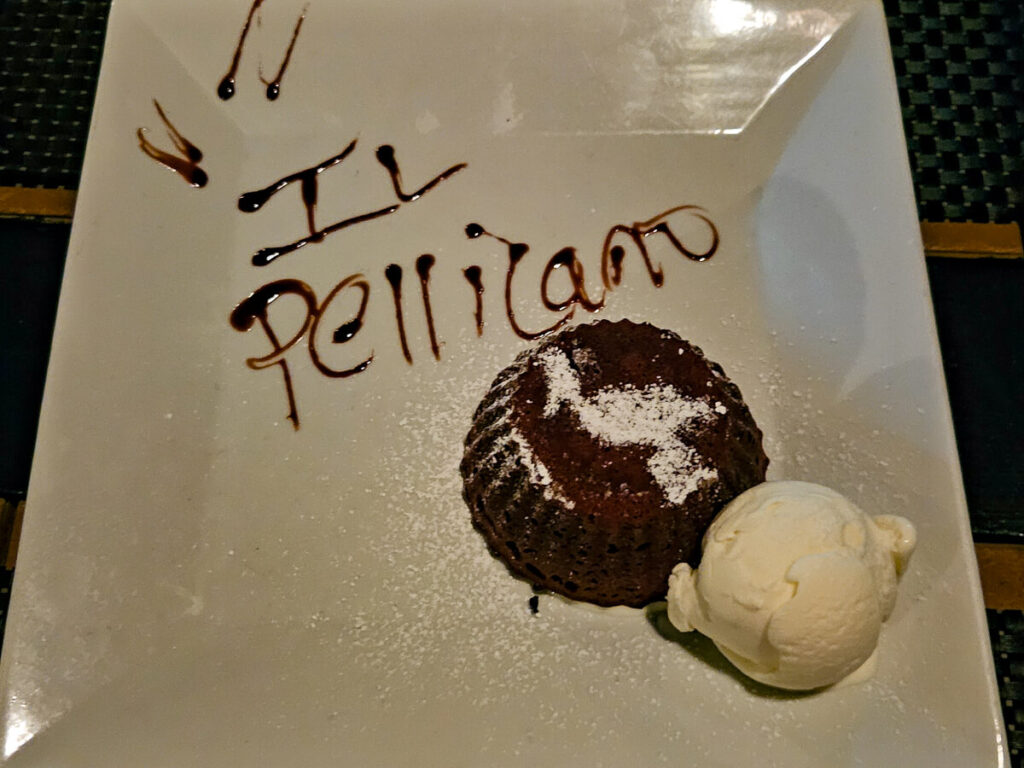 A chocolate fondant with vanilla ice cream. On the plate is the name of the restaurant "Il Pellicano" written with dark chocolate sauce.