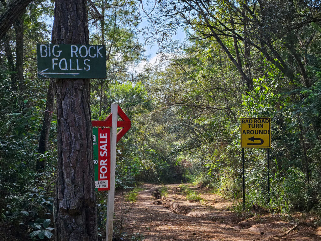 A sign pointing the way to Big Rock Falls, in front of a road sign that tells drivers to turn around as the road is bad.