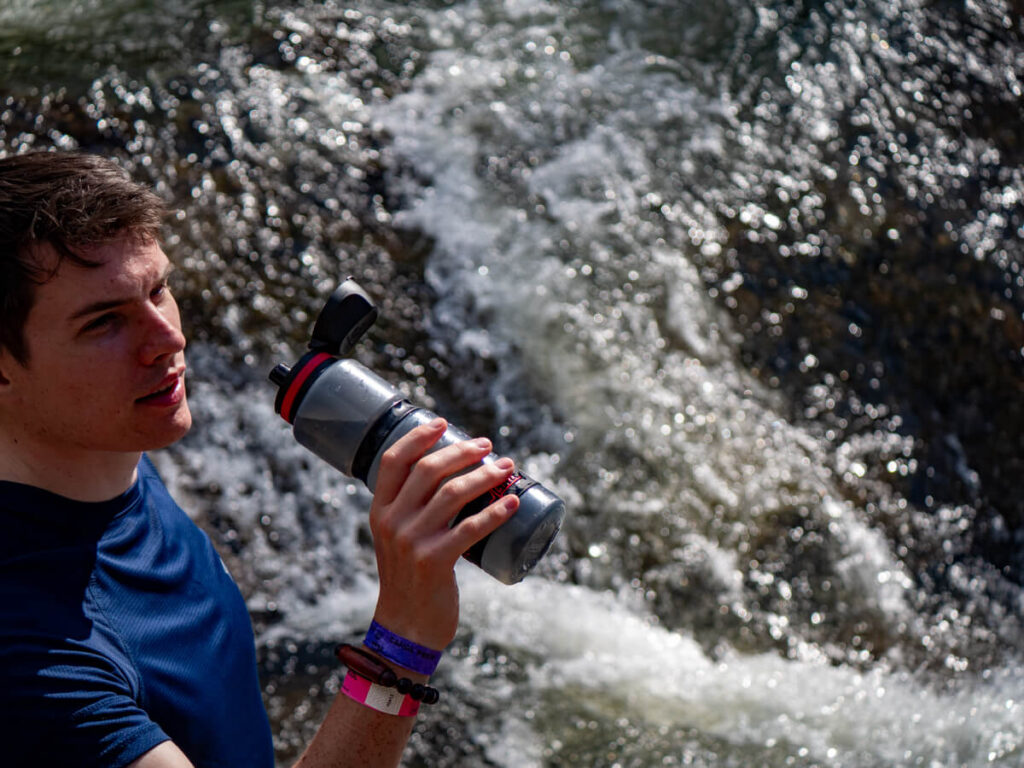 Dan drinking form a reusable filter water bottle in front of a gushing river at Big Rock Falls in Belize's Mountain Pine Ridge Forest Reserve.