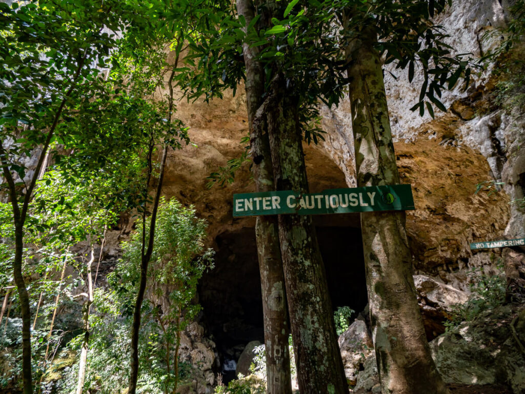 A sign warning visitors to "Enter Cautiously" in front of the entrance to Rio Frio Cave in the Mountain Pine Ridge Forest Reserve.