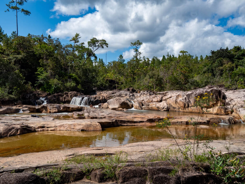A river flowing through boulders and cascading into waterfalls at Rio On Pools swimming hole in Mountain Pine Ridge Forest Reserve.