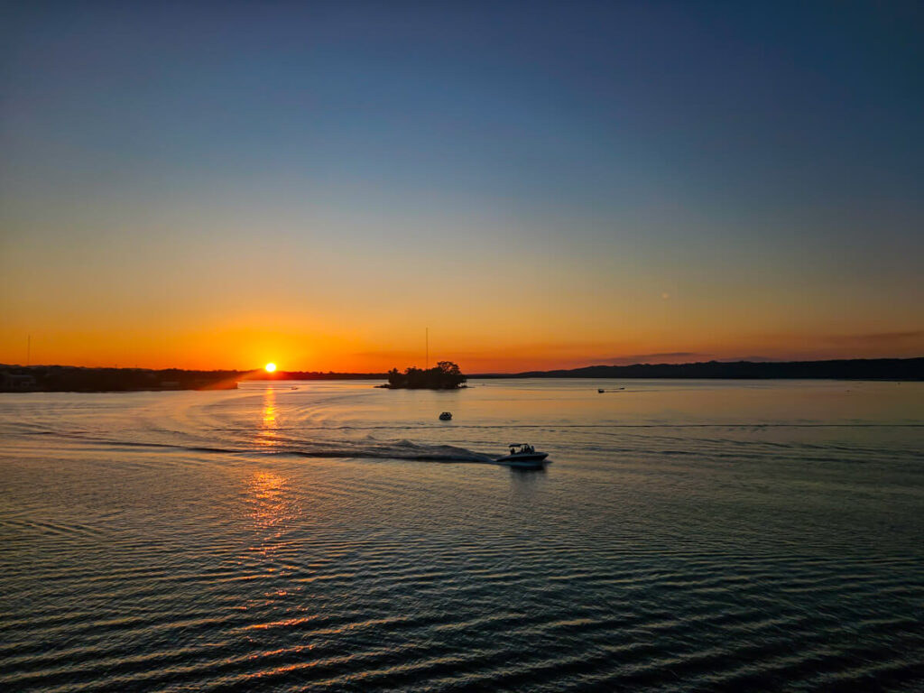 A blazing orange sunset behind Lake Peten Itza with a small lancha sailing in front of an island, seen from Flores, Guatemala.
