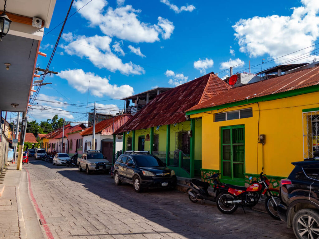 A cobbled street in Flores, Guatemala, lined by colourful houses and parked cars.