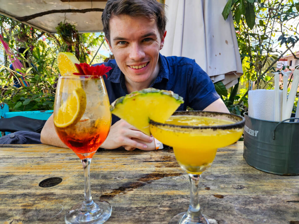 Dan smiling at a table with colourful cocktails in Maracuya, a restaurant in Flores, Guatemala.