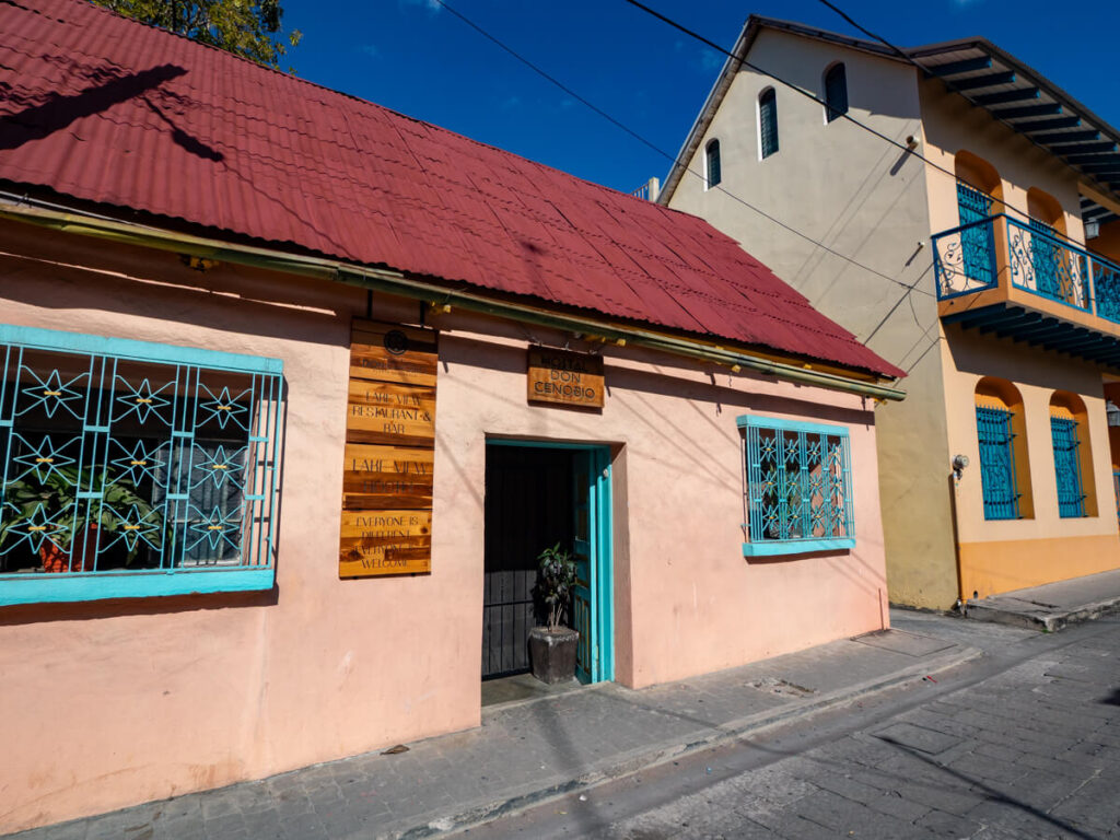 The pink exterior of Hostal Don Cenobio on a sloped, cobbled street in Isla de Flores, Guatemala.