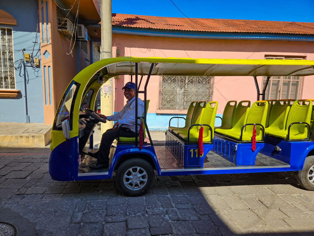 A small blue and yellow, open air tourist shuttle driving the streets of Isla de Flores, Guatemala.