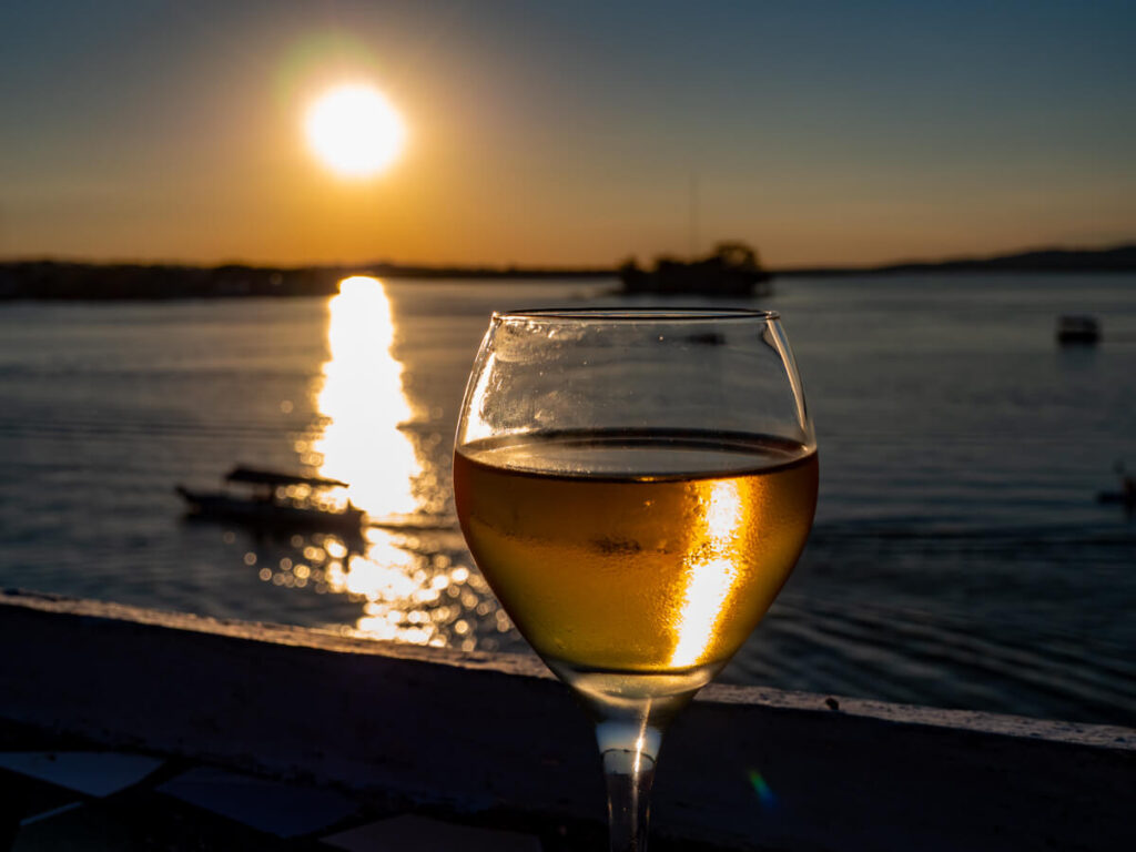A glass of wine on a rooftop bar in front of Lake Peten Itza at sunset in Flores, Guatemala.