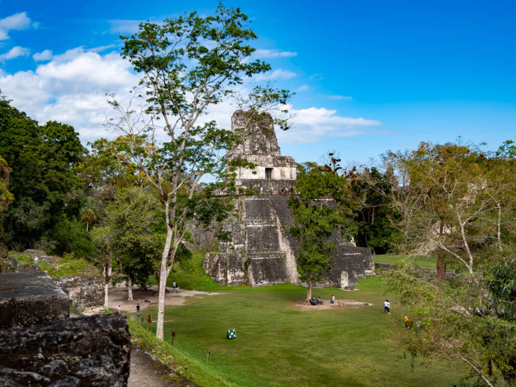 Tour groups exploring a plaza in front of a grand temple in Tikal, Guatemala.