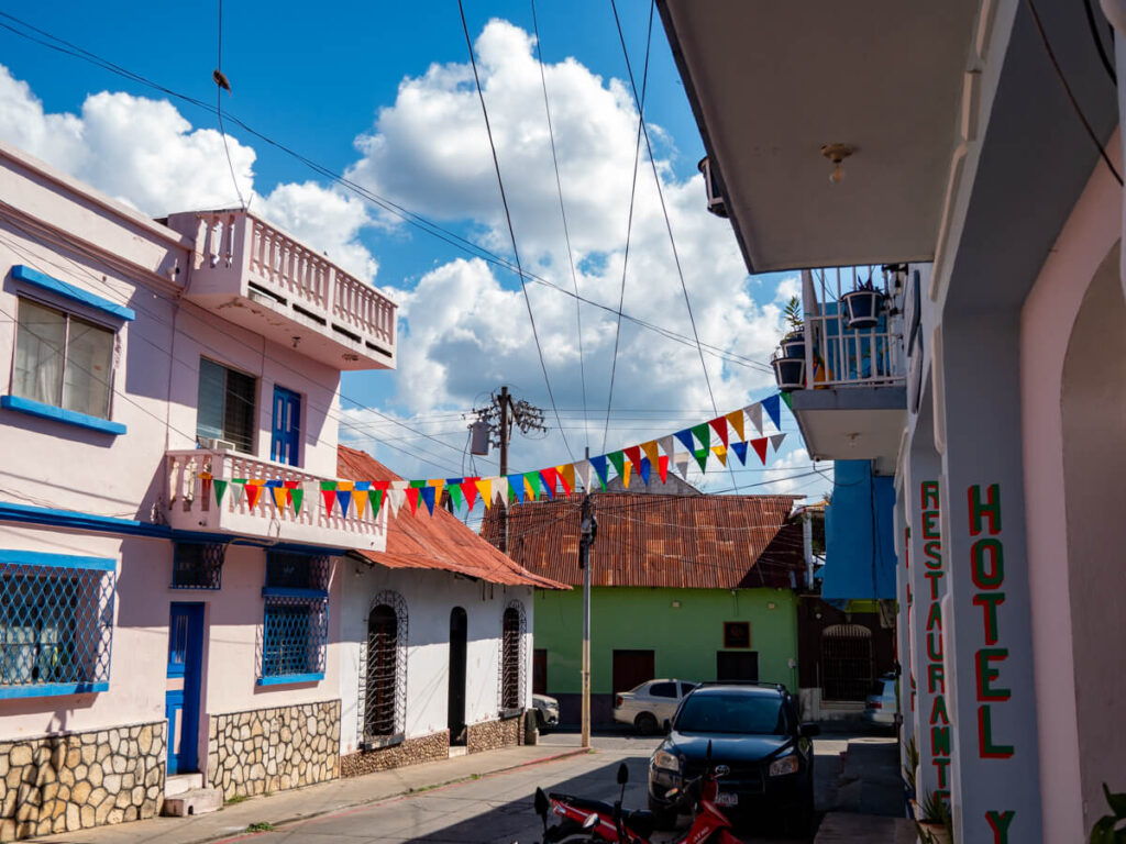 A cobbled street in Flores Island, Guatemala, lined by colourful buildings, hotels, restaurants, and bunting.