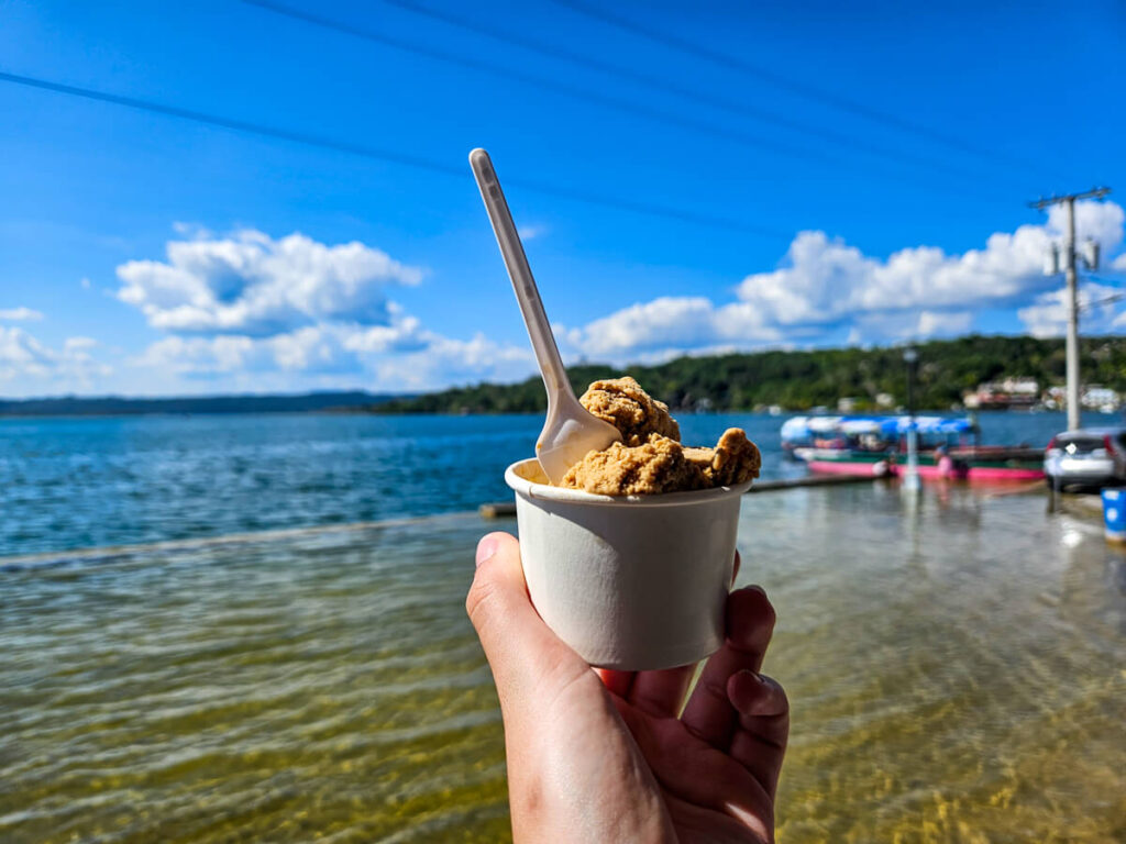 A hand holding a pot of ice cream from Yogulato in Flores in front of Lake Peten Itza.