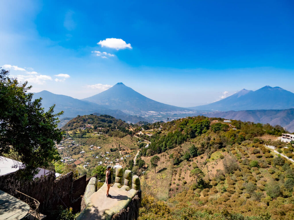 Lucy standing on a giant hand sculpture in front of rolling hills at the eco-park Hobbitenango in Antigua, Guatemala.