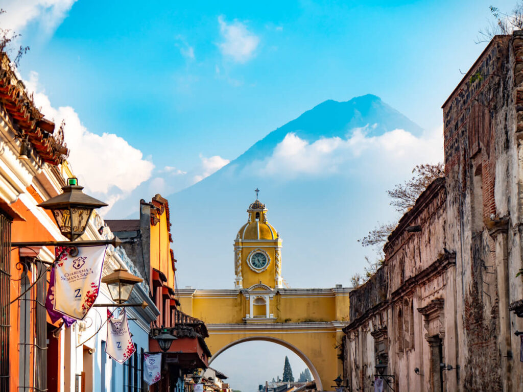A street leading to the yellow Arco de Santa Catalina standing in front of the looming Volcán de Agua in Antigua, Guatemala.
